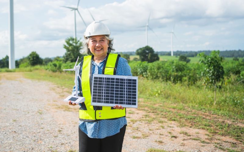 Careers Planner Solar Power Woman holding a solar panel with wind turbines in the background.
